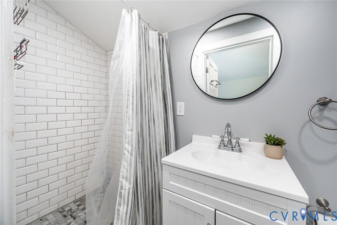 1818 Arlington Road, Hopewell, VA 23860 Bathroom featuring white subway tile shower surround, mosaic tile flooring, white vanity cabinet with integrated countertop, chrome dual-handle faucet, and circular wall-mounted mirror
