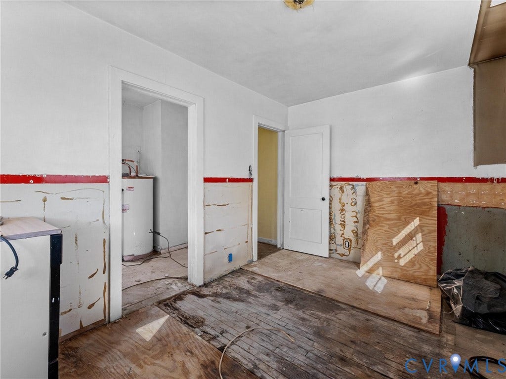 2900 Overton Road, Henrico, VA 23228 Interior space featuring exposed wood subflooring, partially paneled walls, a single-panel interior door, and a dedicated utility area containing a water heater