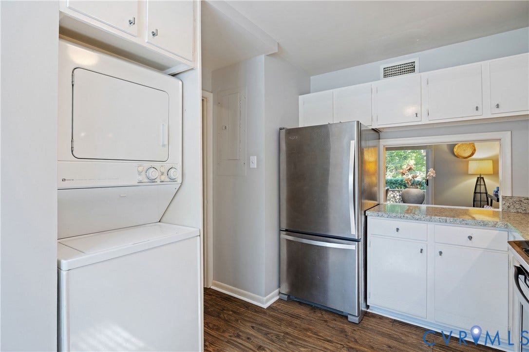 9131 Derbyshire Road, #B, Deerwood Condominiums, Henrico, VA 23229 Stacked laundry center with overhead cabinetry, stainless steel bottom-freezer refrigerator, white shaker-style cabinetry, stone-finish countertops, and wood-finish flooring
