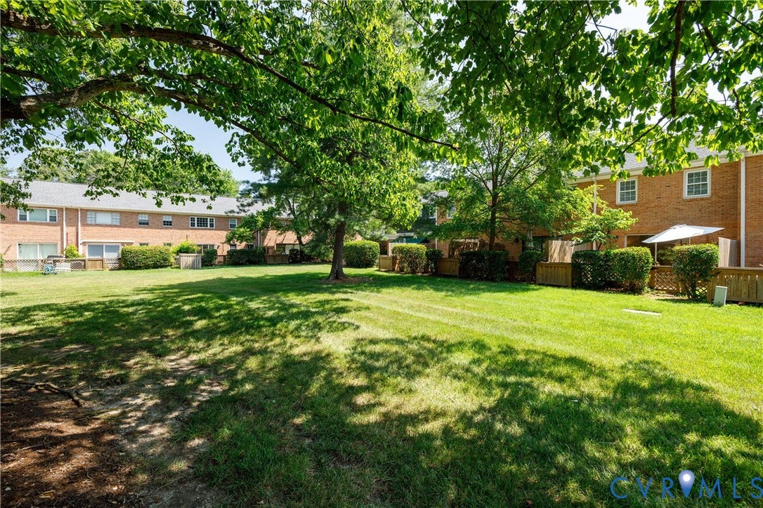 9131 Derbyshire Road, #B, Deerwood Condominiums, Henrico, VA 23229 Expansive shared green space featuring mature shade trees, brick exterior facades, and wood privacy fencing