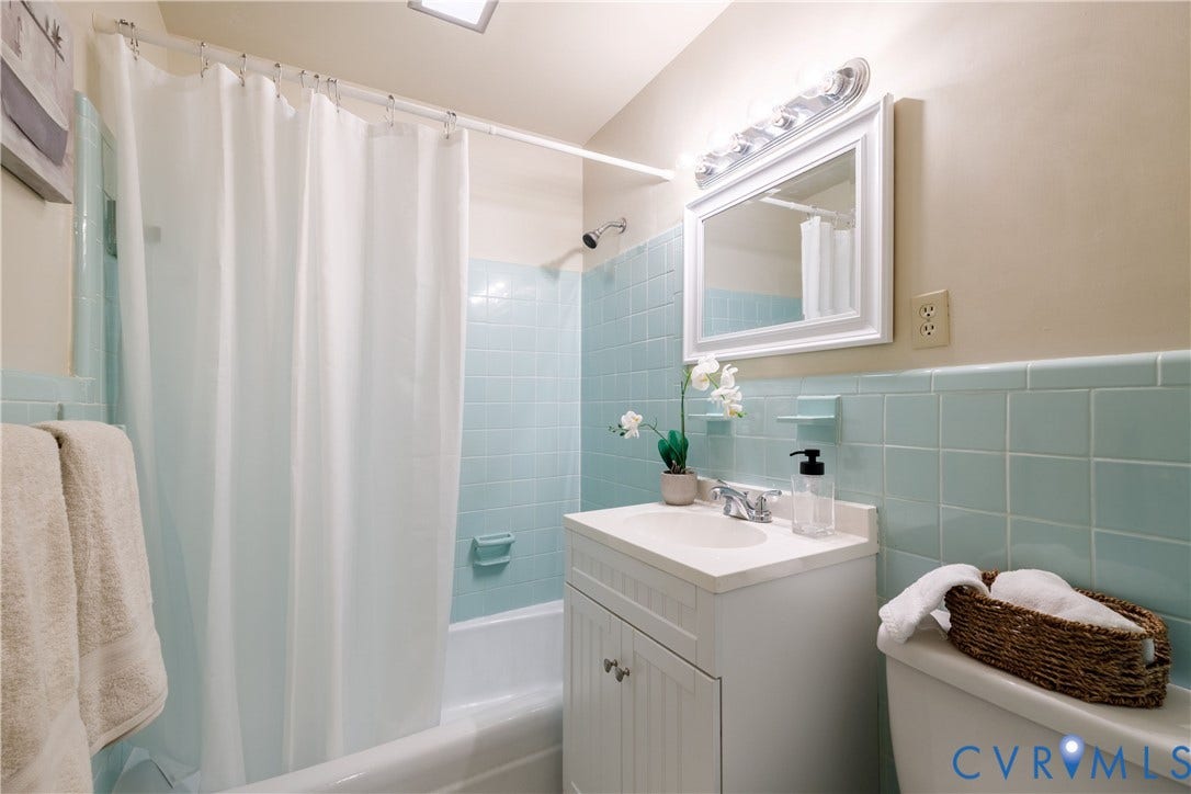 9131 Derbyshire Road, #B, Deerwood Condominiums, Henrico, VA 23229 Bathroom featuring light blue wall tiles, a built-in bathtub with shower head, a white vanity cabinet with a integrated sink, and a framed wall-mounted mirror with integrated lighting