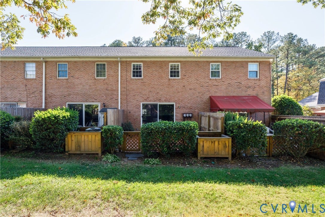 9131 Derbyshire Road, #B, Deerwood Condominiums, Henrico, VA 23229 Brick exterior featuring a wood-fenced outdoor space, a retractable fabric awning, and mature shrubbery