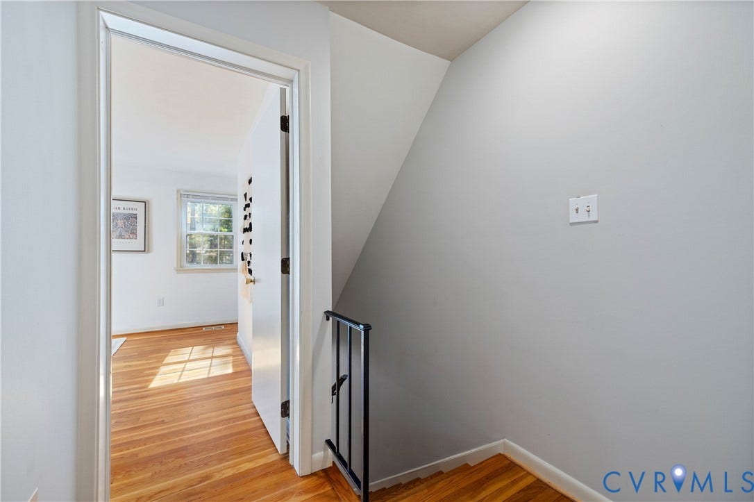 9131 Derbyshire Road, #B, Deerwood Condominiums, Henrico, VA 23229 Staircase featuring wood-finish flooring and a black metal handrail, complemented by a white interior door and neutral wall paint