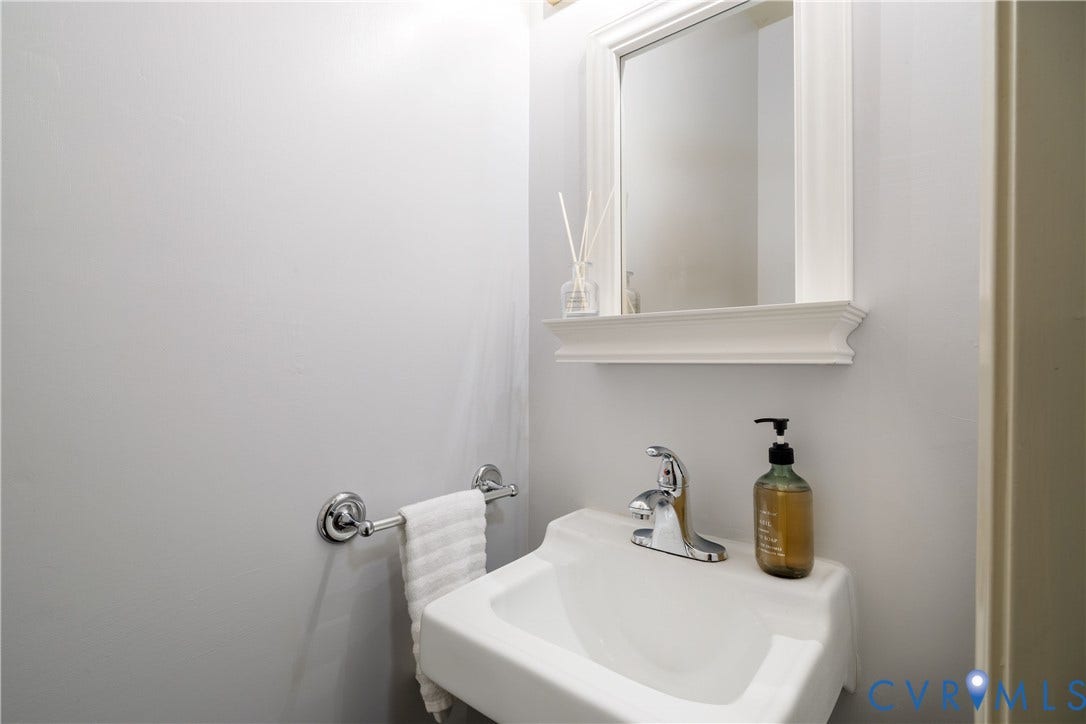 9131 Derbyshire Road, #B, Deerwood Condominiums, Henrico, VA 23229 Wall-mounted white basin sink featuring a chrome faucet, complemented by a framed mirror with an integrated shelf and a chrome towel bar