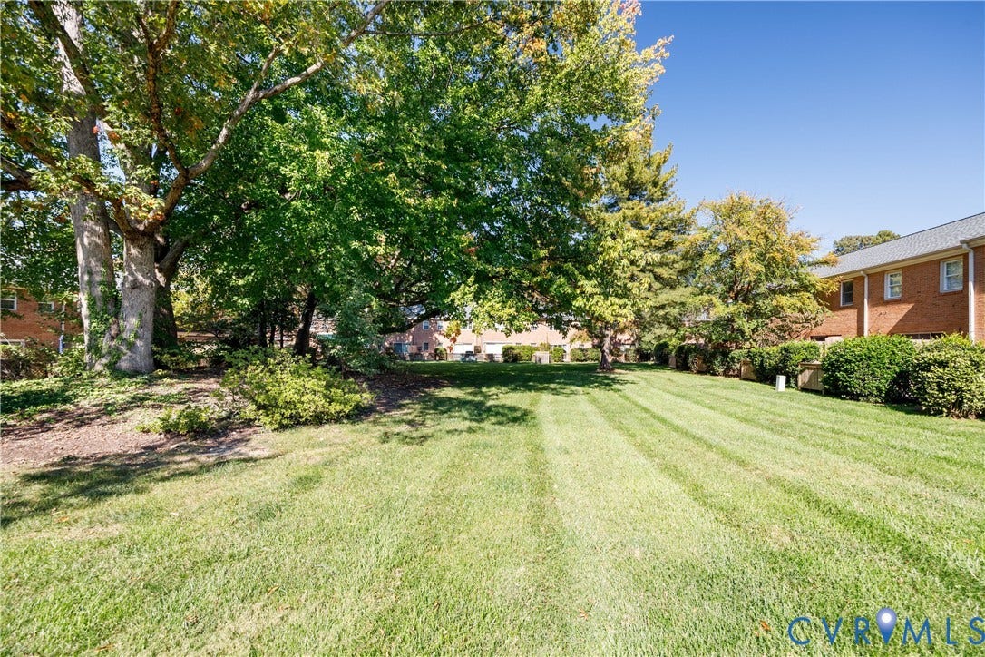 9131 Derbyshire Road, #B, Deerwood Condominiums, Henrico, VA 23229 Expansive lawn area featuring mature trees, manicured shrubs, and brick exterior structures