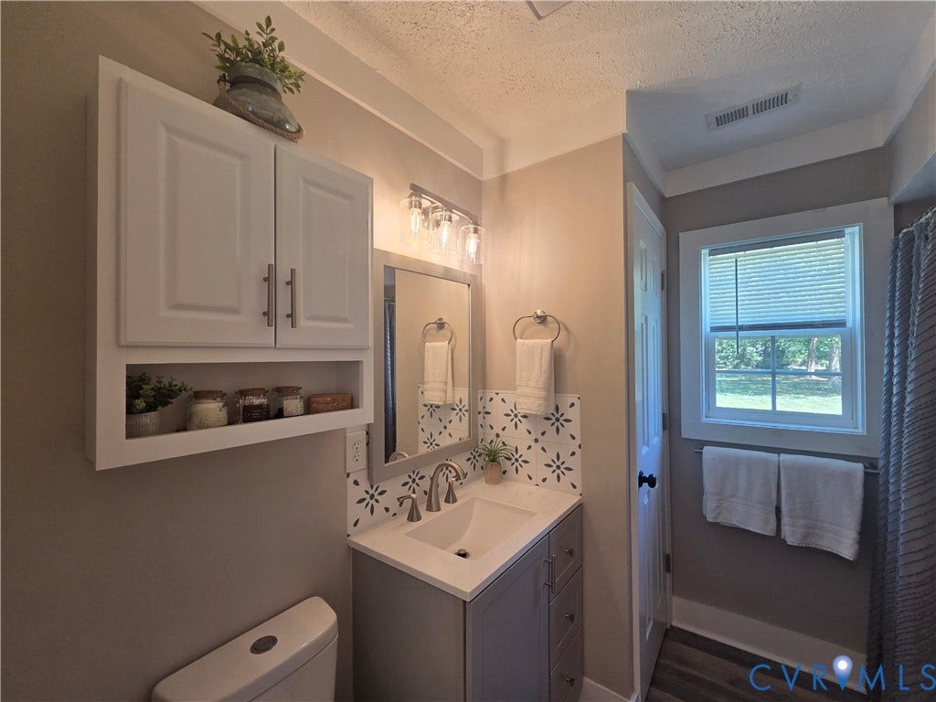 7620 Cypress Drive, Lanexa, VA 23089 Bathroom vanity featuring a quartz-finish countertop, undermount sink, patterned tile backsplash, white wall-mounted storage cabinetry, and brushed nickel hardware