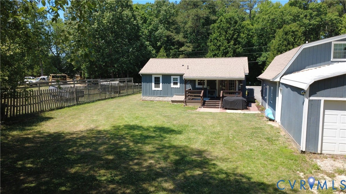 7620 Cypress Drive, Lanexa, VA 23089 Rear exterior featuring vertical siding, a wood deck with stairs, a paved patio area, an attached garage structure, and a fenced backyard
