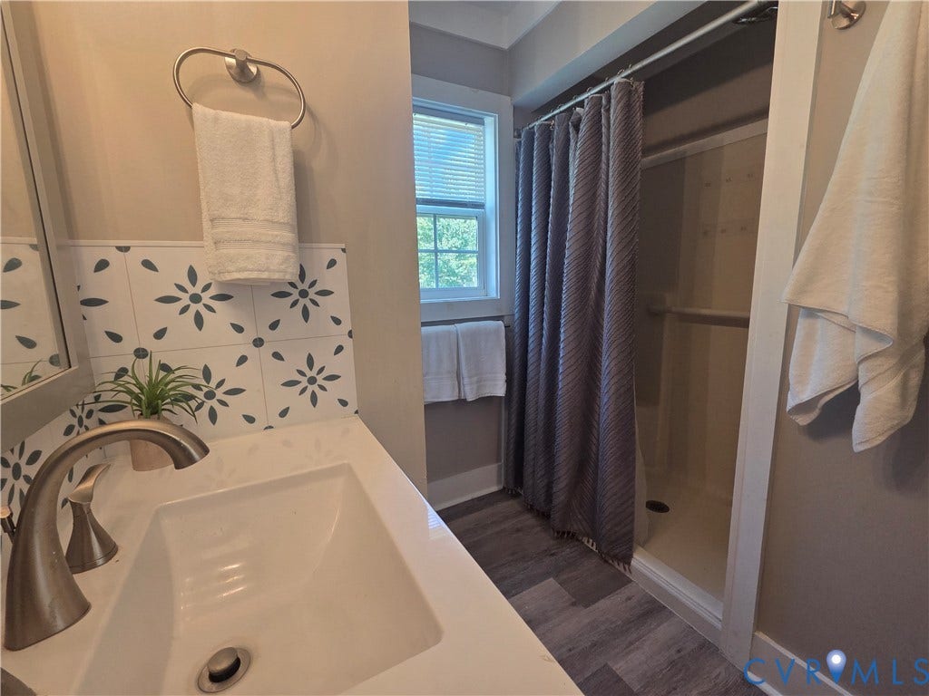 7620 Cypress Drive, Lanexa, VA 23089 Bathroom featuring a vanity with a white countertop, patterned tile backsplash, integrated sink, metal faucet, and a shower stall with wood-finish flooring
