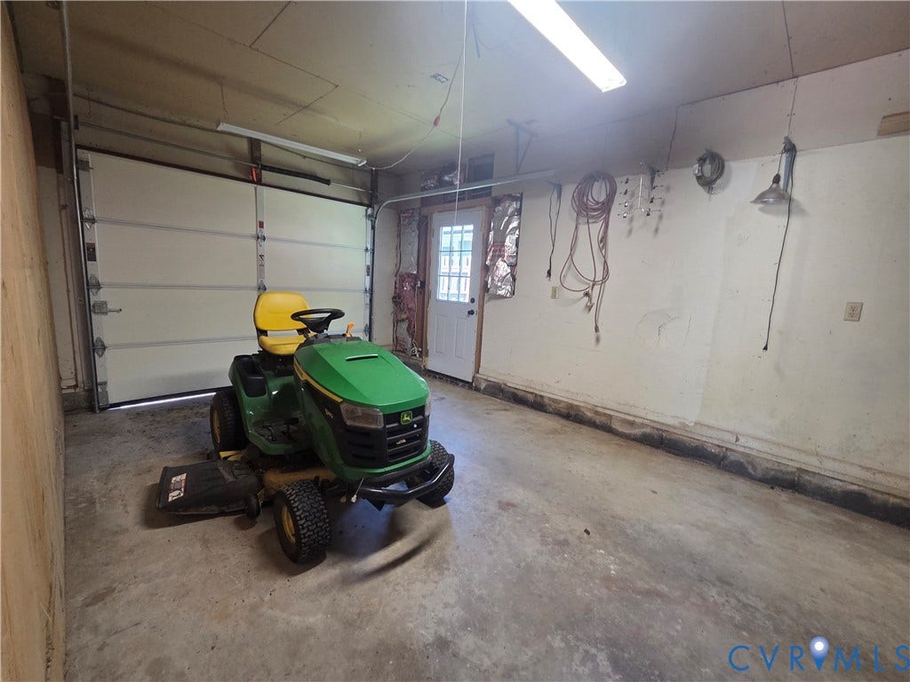 7620 Cypress Drive, Lanexa, VA 23089 Garage space featuring a concrete floor, sectional overhead door, exterior-access door with a glass inlay, and interior wall-mounted lighting