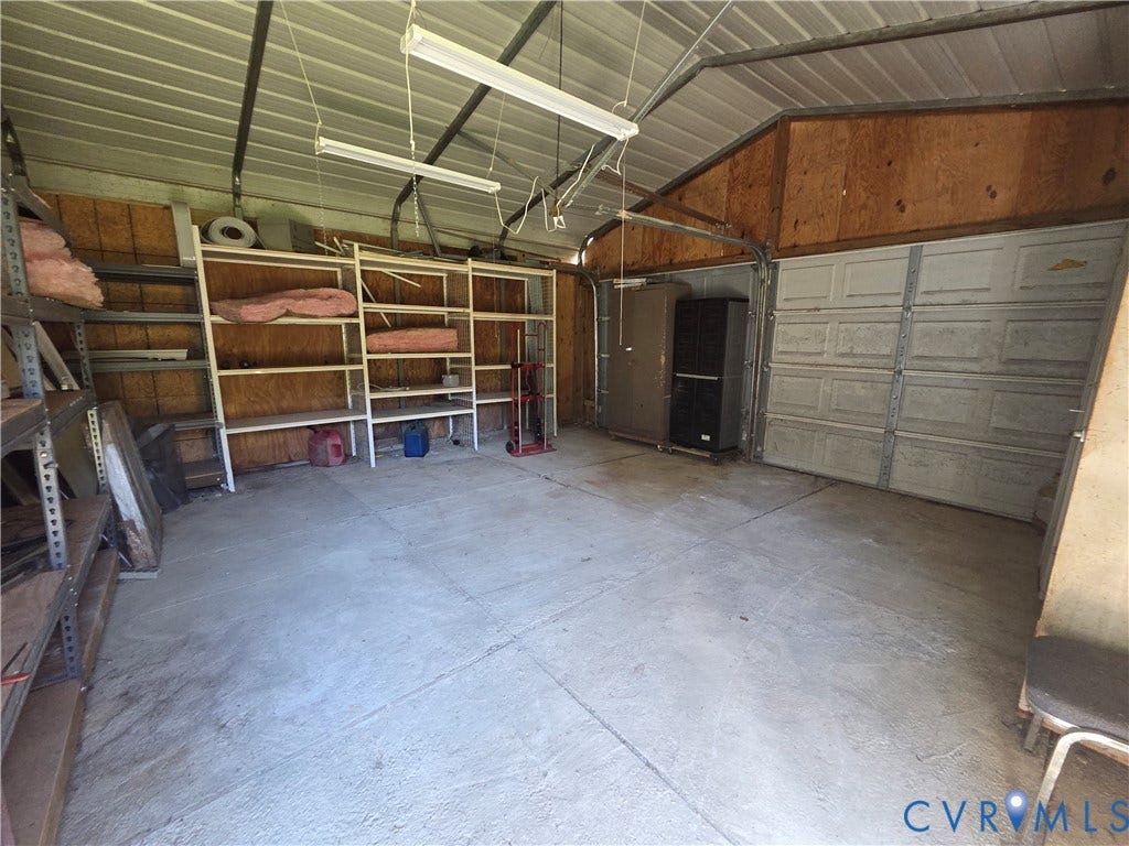 7620 Cypress Drive, Lanexa, VA 23089 Detached garage featuring a concrete floor, plywood wall paneling, overhead fluorescent lighting, and a metal roll-up door