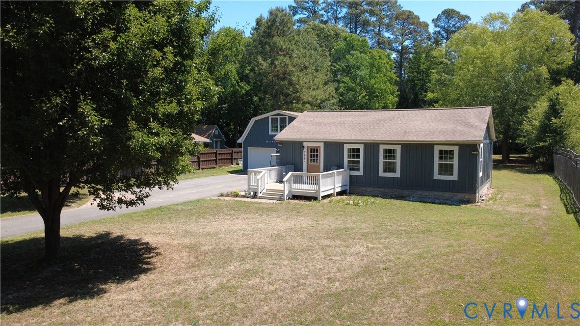 7620 Cypress Drive, Lanexa, VA 23089 Vertical board-and-batten siding, white-railed entrance deck, asphalt shingle roof, paved driveway, and detached barn-style garage
