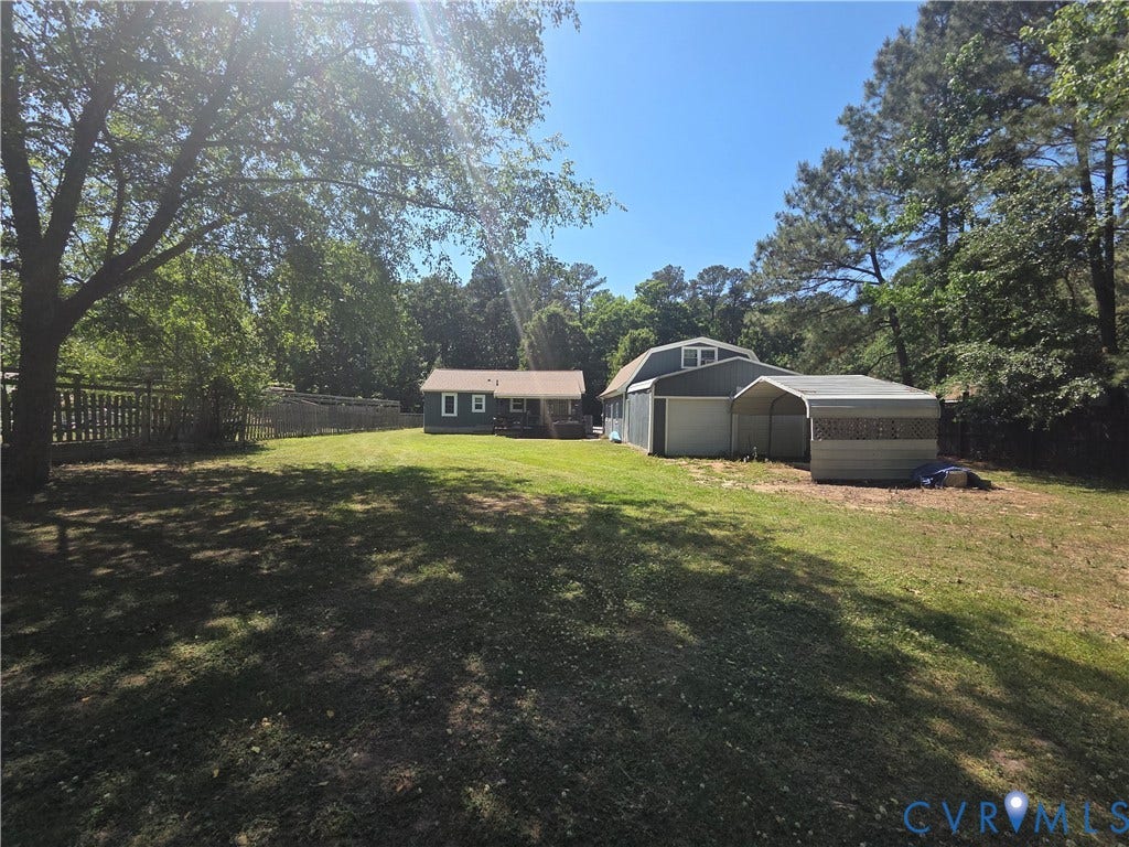 7620 Cypress Drive, Lanexa, VA 23089 Expansive backyard featuring mature trees, a fenced perimeter, a detached two-story garage, and a metal carport