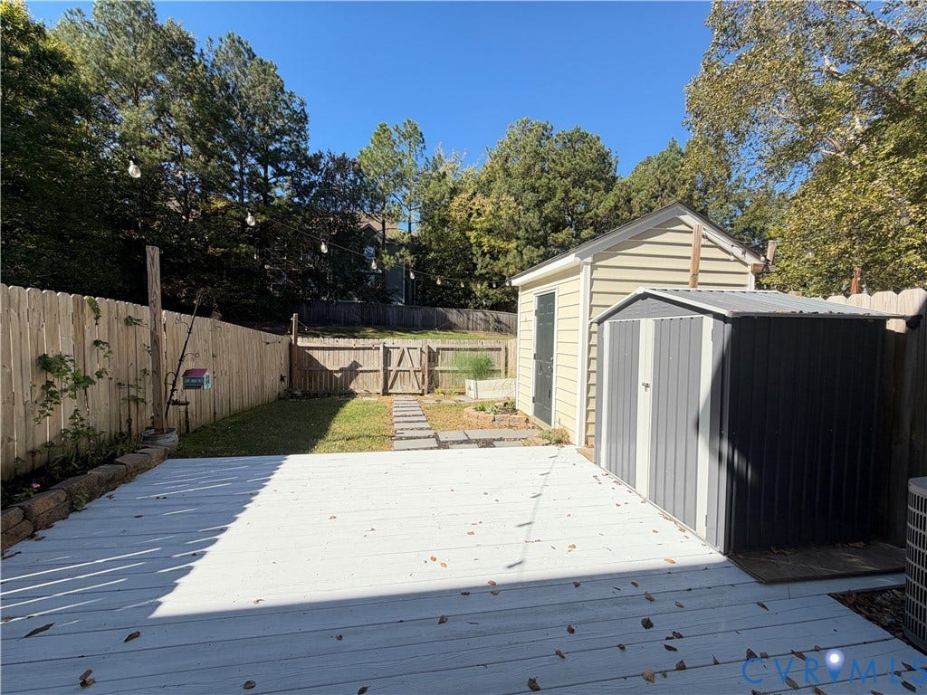3105 Friars Walk Lane, Glen Allen, VA 23059 Fenced backyard featuring a painted deck, stone paver pathway, elevated garden bed, and two detached storage structures