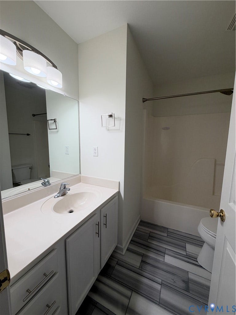 3105 Friars Walk Lane, Glen Allen, VA 23059 Bathroom vanity with integrated sink, stone-finish countertop, multilight vanity fixture, and full-width mirror, featuring wood-finish floor tiling and a combined tub and shower enclosure