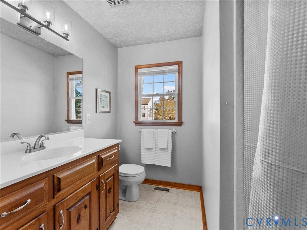 209 Taraby Drive, Hunters Run, Sandston, VA 23150 Bathroom featuring a wooden vanity with a solid-surface countertop, an integrated sink, a full-width wall mirror, and a single-hung window with wood-finish trim