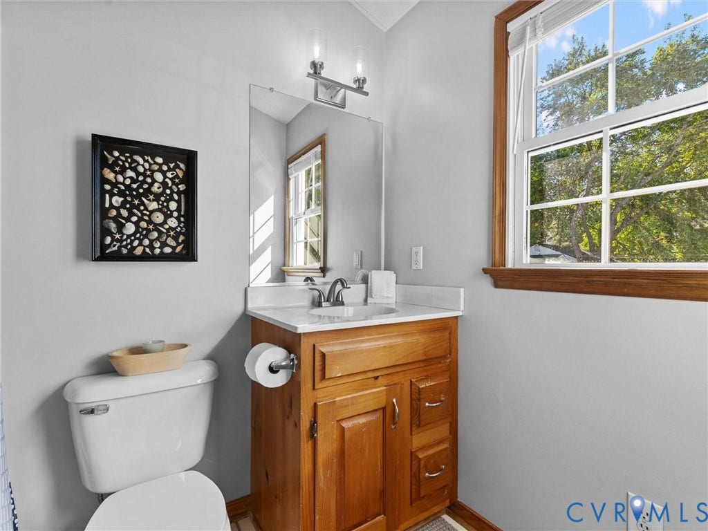 209 Taraby Drive, Hunters Run, Sandston, VA 23150 Bathroom featuring a natural wood-finish vanity, light-toned countertop with an integrated sink, polished metal dual-handle faucet, wall-mounted vanity light, and a double-hung window with wood trim