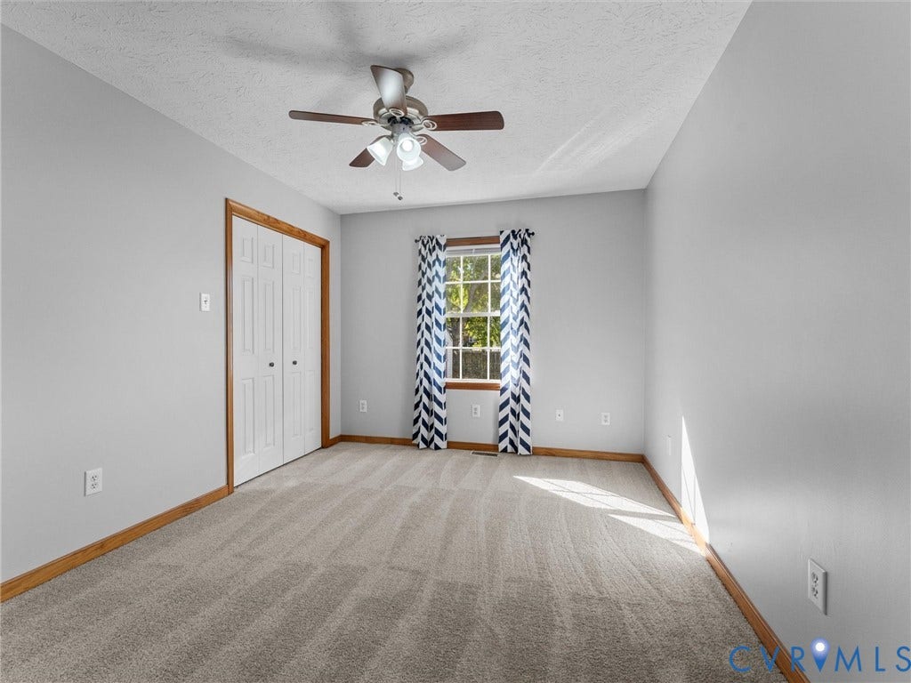 209 Taraby Drive, Hunters Run, Sandston, VA 23150 Neutral-toned carpeted flooring, wall-mounted ceiling fan with integrated lighting, dual-panel closet doors with wood trim, and a window with wood framing