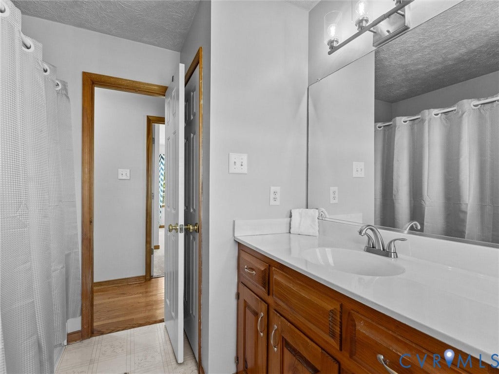 209 Taraby Drive, Hunters Run, Sandston, VA 23150 Bathroom featuring a vanity with wood-finish cabinetry, an integrated sink with a chrome dual-handle faucet, a full-width mirror, and a wall-mounted light fixture