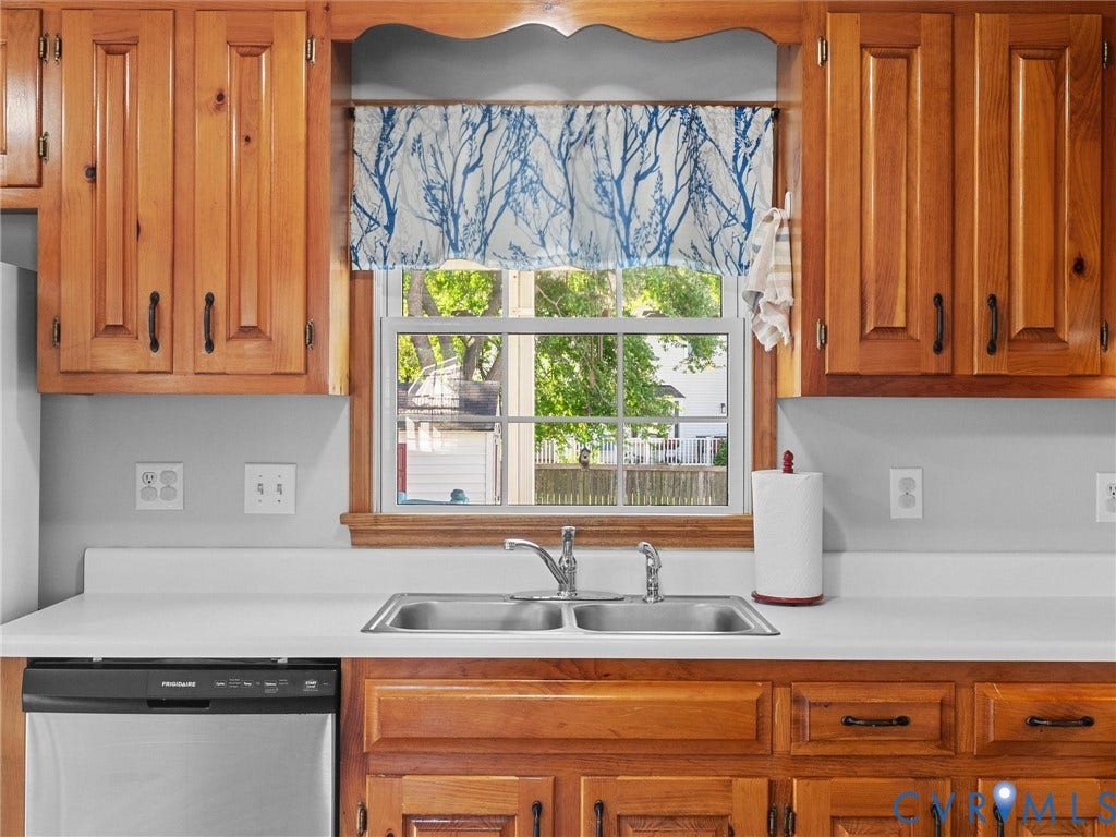 209 Taraby Drive, Hunters Run, Sandston, VA 23150 Natural wood cabinetry, white solid-surface countertops, dual-basin stainless steel sink with chrome faucet, and multi-pane window
