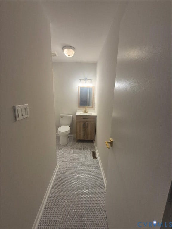 17 Jarratt Court, Petersburg, VA 23803 Restroom featuring penny tile flooring, a wood-finish vanity with a stone countertop, a brass-tone faucet, and a wall-mounted vanity light
