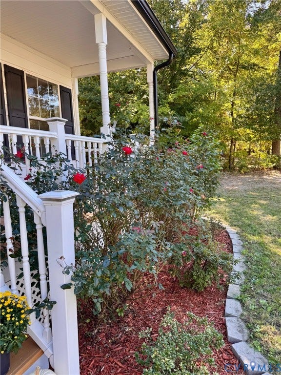 10984 Elmont Woods Drive, Elmont, Glen Allen, VA 23059 Covered porch featuring white wooden railings, columns, and a landscaped garden bed with rose bushes, decorative mulch, and stone edging