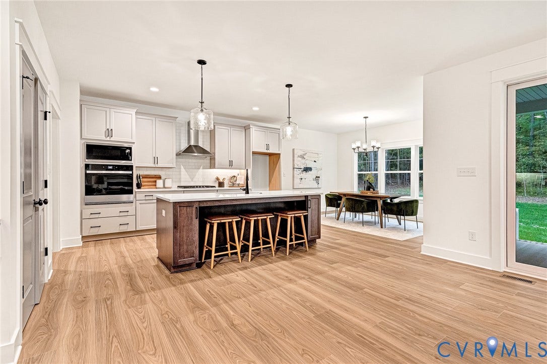 9107 Terroir Lane, Viniterra Villas, New Kent, VA 23124 Kitchen featuring wood-finish flooring, a central island with a contrasting dark finish, white cabinetry, integrated stainless steel appliances, and glass pendant lighting