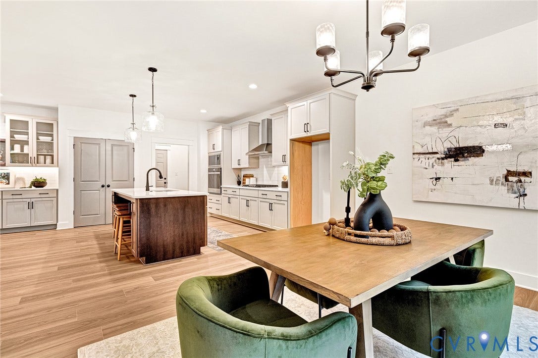 9107 Terroir Lane, Viniterra Villas, New Kent, VA 23124 Kitchen featuring wood-finish flooring, a central island with a contrasting dark wood base and stone countertop, light-colored shaker-style cabinetry, a stainless steel wall oven, and a five-light chandelier