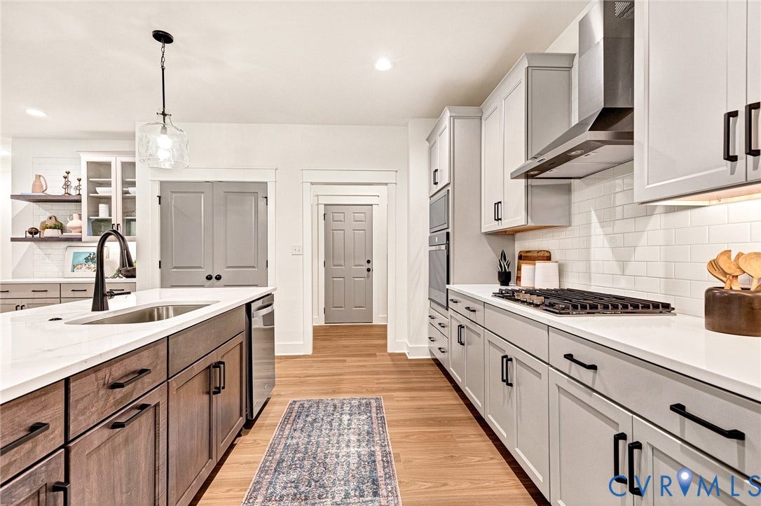 9107 Terroir Lane, Viniterra Villas, New Kent, VA 23124 Kitchen featuring light-toned cabinetry, a central island with a stainless steel sink, solid-surface countertops, white tile backsplash, and wood-finish flooring