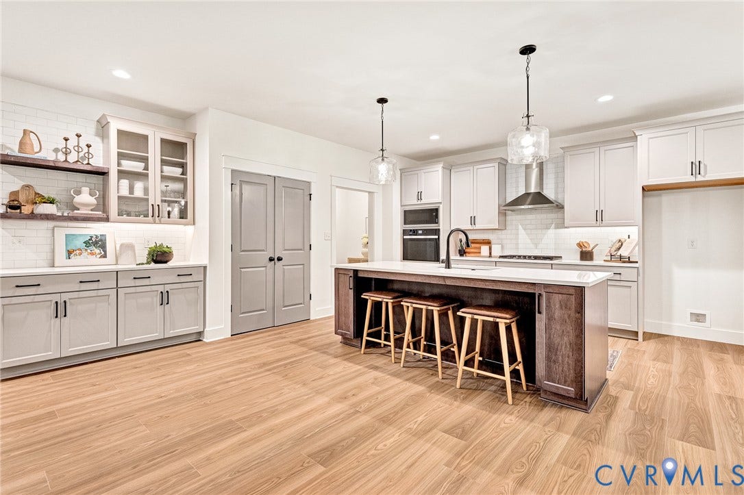 9107 Terroir Lane, Viniterra Villas, New Kent, VA 23124 Kitchen featuring shaker-style cabinetry, a central island with countertop seating, stainless steel appliances, subway tile backsplash, and wood-finish flooring