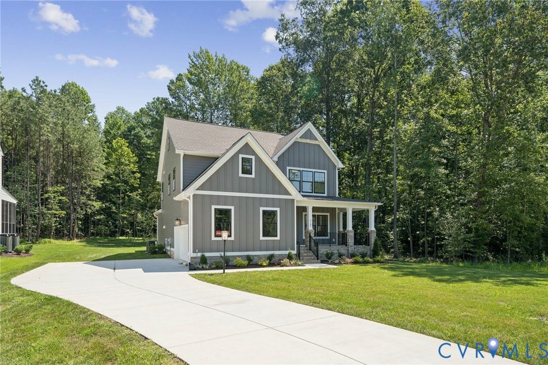 9107 Terroir Lane, Viniterra Villas, New Kent, VA 23124 Two-story residence featuring vertical board-and-batten siding, a covered front porch with stone pillar accents, a multi-gabled roofline, and a concrete driveway