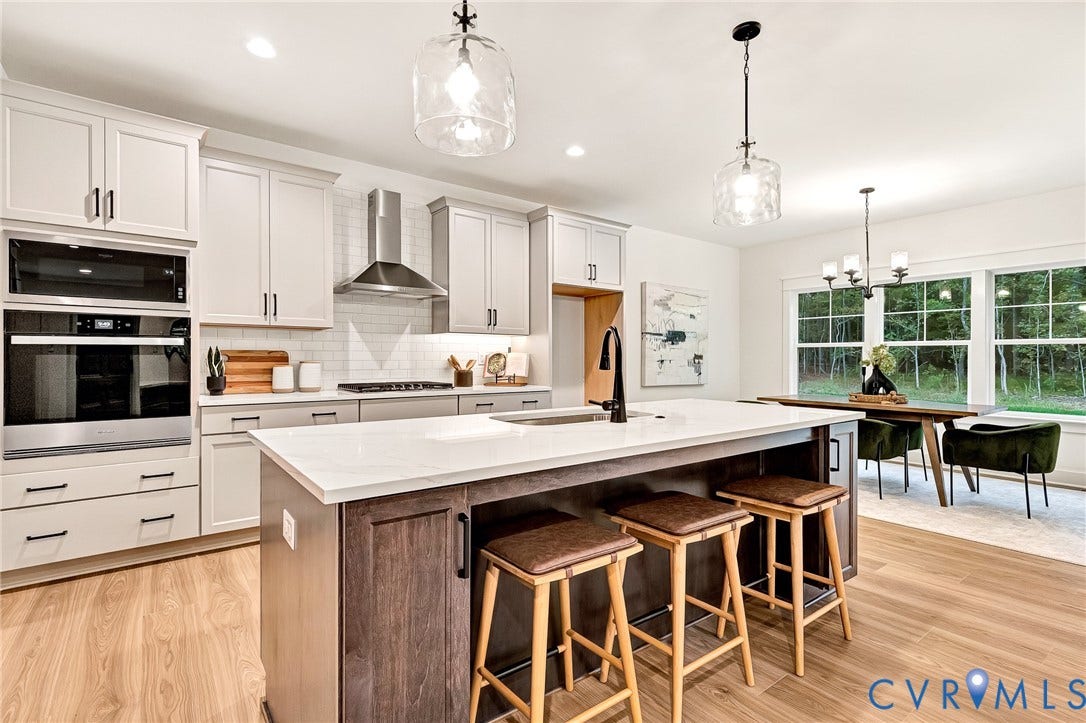 9107 Terroir Lane, Viniterra Villas, New Kent, VA 23124 Kitchen featuring shaker-style cabinetry, a central island with a solid surface countertop, stainless steel built-in double ovens, a glass-tiled backsplash, and wood-finish flooring
