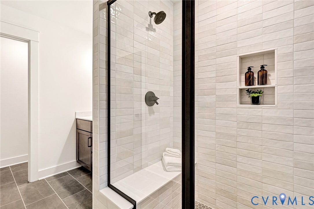 9107 Terroir Lane, Viniterra Villas, New Kent, VA 23124 Walk-in shower featuring white subway-style wall tile, a built-in tiled bench, a recessed shower niche, and matte black fixtures, enclosed by a black-framed glass partition