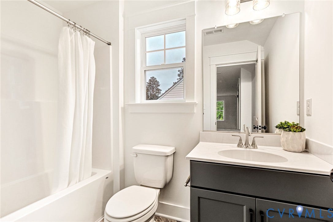 9107 Terroir Lane, Viniterra Villas, New Kent, VA 23124 Bathroom featuring a dark-toned vanity with a light-colored countertop, integrated sink, large wall-mounted mirror, and a combination tub and shower with white surround