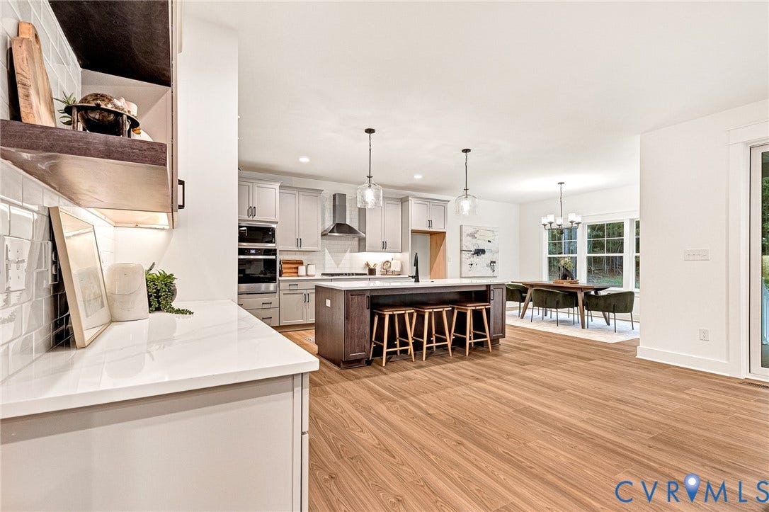 9107 Terroir Lane, Viniterra Villas, New Kent, VA 23124 Kitchen featuring light cabinetry, a contrasting dark wood kitchen island, wood-finish flooring, white subway tile backsplash, and stainless steel built-in appliances