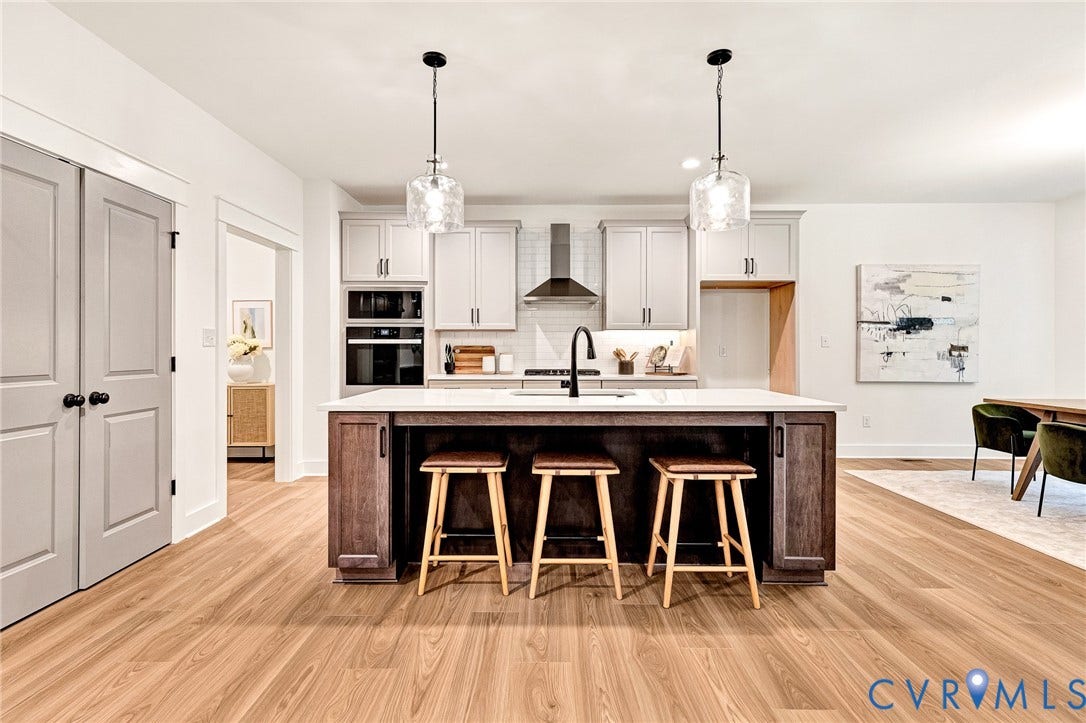 9107 Terroir Lane, Viniterra Villas, New Kent, VA 23124 Kitchen featuring a center island with a stone-finish countertop, stainless steel wall-mounted oven and microwave, custom cabinetry, wood-finish flooring, and dual glass pendant light fixtures
