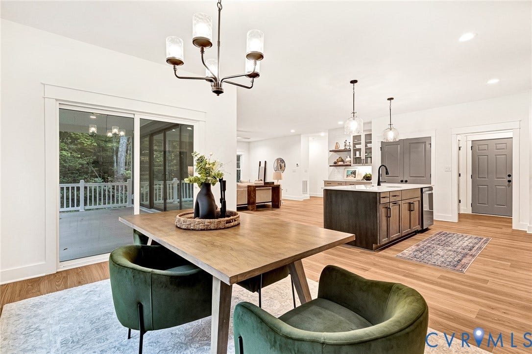 9107 Terroir Lane, Viniterra Villas, New Kent, VA 23124 Open-concept interior featuring wood-finish flooring, a kitchen island with dark cabinetry, sliding glass doors to a covered deck, and decorative multi-light chandeliers