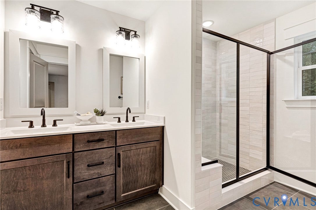 9107 Terroir Lane, Viniterra Villas, New Kent, VA 23124 Double vanity featuring stained wood cabinetry, quartz countertops, matte black fixtures, and a walk-in shower with a glass enclosure and tiled surround