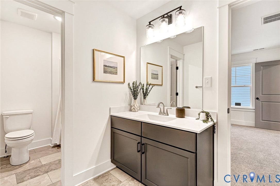 9107 Terroir Lane, Viniterra Villas, New Kent, VA 23124 Bathroom featuring a vanity with dark cabinetry, white solid-surface countertop, rectangular undermount sink, and three-light wall-mounted fixture