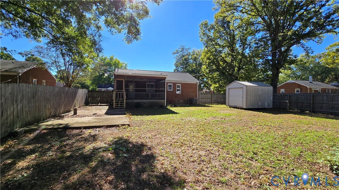 38 Eastlake Drive, Sandston, Sandston, VA 23150 Rear exterior featuring a brick facade, covered porch with wooden railings, concrete patio, detached metal storage shed, and full wood privacy fencing