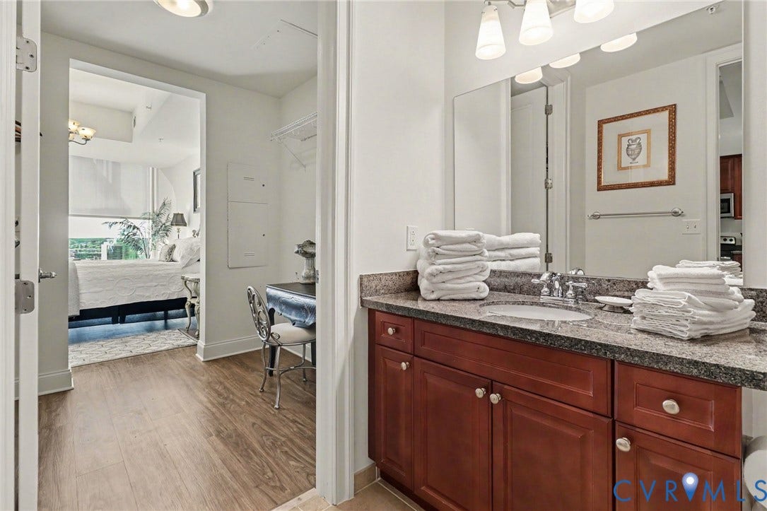 301 Virginia Street, #U1712, Richmond, VA 23219 Bathroom vanity featuring stained wood cabinetry, stone countertop, integrated sink, and full-width wall-mounted mirror