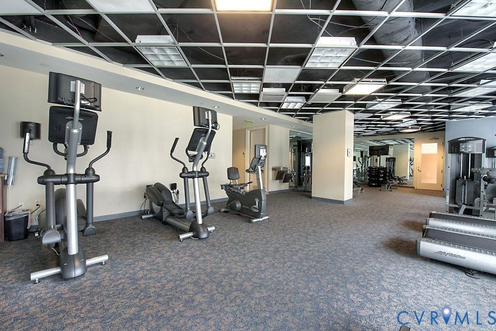 301 Virginia Street, #U1712, Richmond, VA 23219 Fitness space featuring a suspended grid ceiling with integrated lighting, neutral wall finishes, patterned carpeting, and built-in mirrored walls