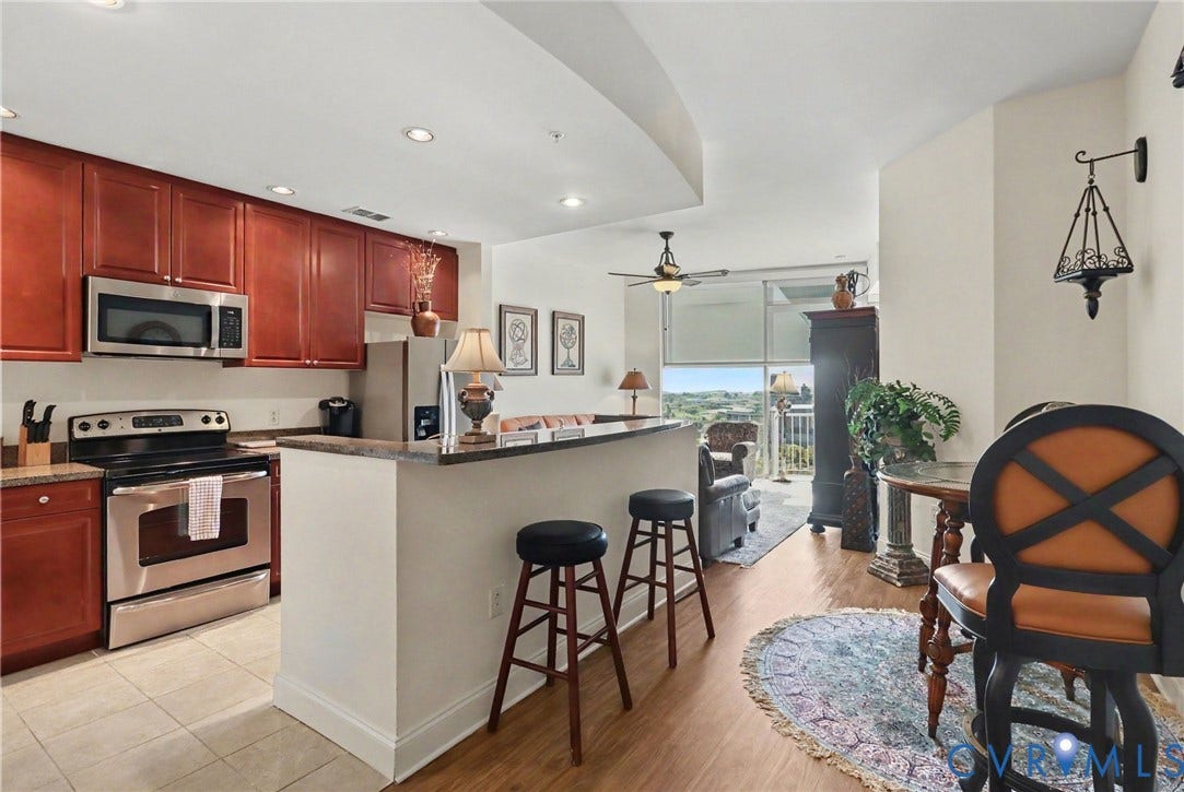 301 Virginia Street, #U1712, Richmond, VA 23219 Kitchen featuring stained wood cabinetry, a breakfast bar with stone-surface countertop, stainless steel appliances, tile flooring, and floor-to-ceiling windows