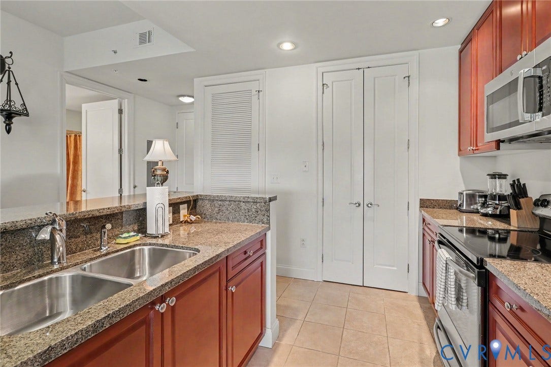 301 Virginia Street, #U1712, Richmond, VA 23219 Kitchen featuring cherry-finish cabinetry, stone-surfaced countertops, a dual-basin stainless steel sink with a high-arch faucet, tile flooring, and recessed lighting