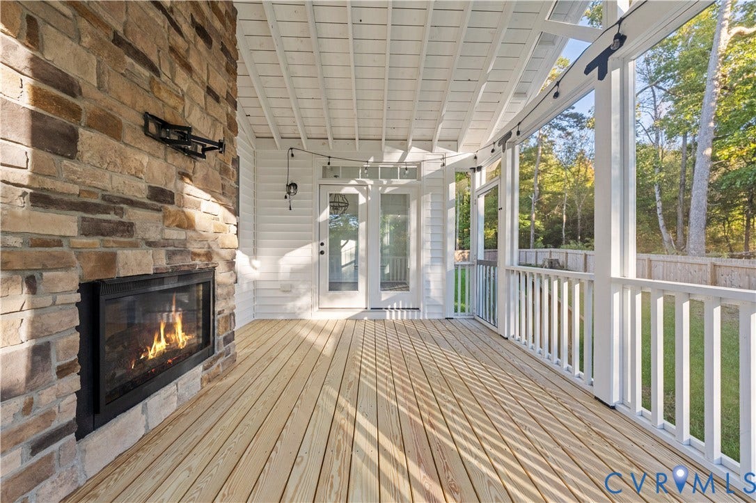 2613 Lilybank Place, NewMarket At RounTrey, Midlothian, VA 23112 Covered porch featuring a wood-plank deck, stone-veneer fireplace with a built-in insert, white horizontal siding, and white wooden railing