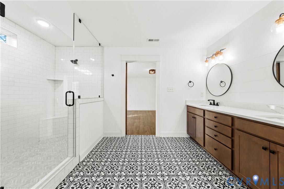2613 Lilybank Place, NewMarket At RounTrey, Midlothian, VA 23112 Bathroom featuring a double-sink vanity with wood cabinetry, a glass-enclosed shower with subway tile surround, patterned tile flooring, and round wall-mounted mirrors