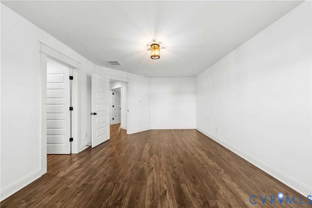 2613 Lilybank Place, NewMarket At RounTrey, Midlothian, VA 23112 Room featuring wood-finish flooring, white walls, four-panel interior doors with matte black hardware, and a center-mounted ceiling light fixture