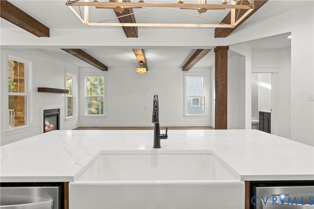 2613 Lilybank Place, NewMarket At RounTrey, Midlothian, VA 23112 Kitchen featuring a large waterfall-edge countertop, white farmhouse sink, matte black gooseneck faucet, exposed wooden ceiling beams, and a fireplace with a wooden mantel