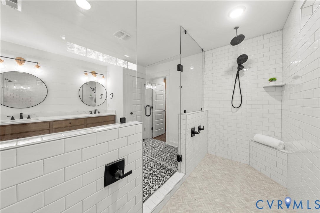 2613 Lilybank Place, NewMarket At RounTrey, Midlothian, VA 23112 Bathroom featuring a double vanity with wood-finish cabinetry, white subway tile shower enclosure with built-in bench, matte black rainfall showerhead with handheld sprayer, glass shower partition, and decorative patterned floor tiling