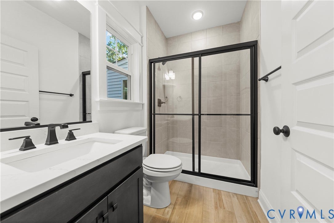 2613 Lilybank Place, NewMarket At RounTrey, Midlothian, VA 23112 Bathroom featuring a vanity with a white countertop, matte black fixtures, wood-finish flooring, and a glass-enclosed shower with tiled surround