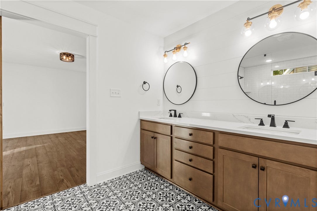 2613 Lilybank Place, NewMarket At RounTrey, Midlothian, VA 23112 Double vanity with wood-finish cabinetry, solid-surface countertops, circular wall-mounted mirrors, matte black fixtures, and patterned tile flooring